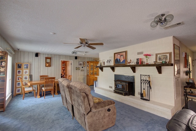 living room with carpet, ceiling fan, a textured ceiling, and a wood stove