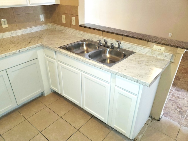 kitchen featuring white cabinets, backsplash, light stone countertops, sink, and light tile floors