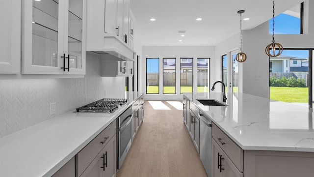 kitchen featuring light stone countertops, appliances with stainless steel finishes, light wood-type flooring, sink, and hanging light fixtures