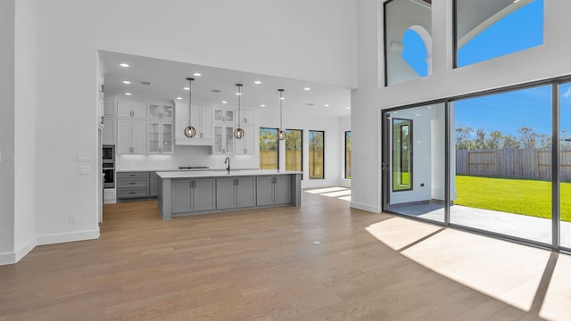 kitchen with gray cabinetry, sink, decorative light fixtures, a high ceiling, and an island with sink