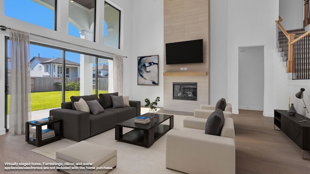 living room with a large fireplace, wood-type flooring, and a towering ceiling