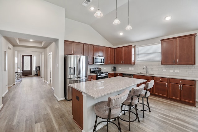 kitchen with sink, light stone counters, a breakfast bar area, a kitchen island, and appliances with stainless steel finishes