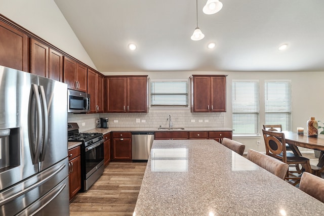 kitchen with sink, stainless steel appliances, vaulted ceiling, decorative light fixtures, and hardwood / wood-style flooring