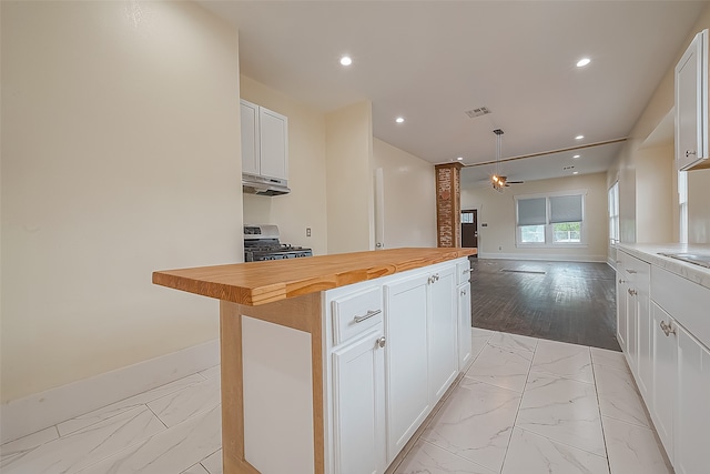 kitchen featuring stainless steel range, butcher block countertops, a center island, white cabinets, and light hardwood / wood-style floors