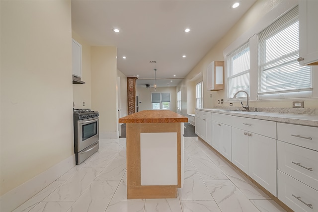 kitchen with stainless steel gas range, white cabinetry, wooden counters, a center island, and sink