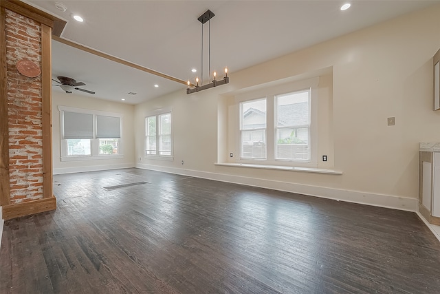 unfurnished living room featuring ceiling fan with notable chandelier, plenty of natural light, and dark hardwood / wood-style flooring