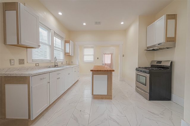 kitchen with white cabinetry, stainless steel gas range, a kitchen island, and sink