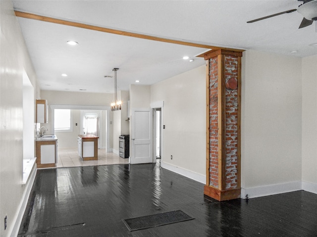 unfurnished living room featuring ornate columns, ceiling fan with notable chandelier, sink, and light hardwood / wood-style flooring