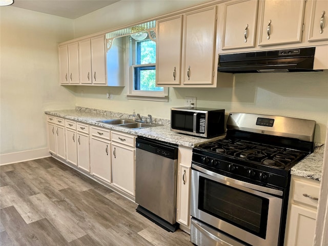 kitchen with light stone counters, appliances with stainless steel finishes, sink, and light hardwood / wood-style floors