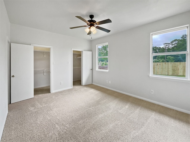 unfurnished bedroom with a walk in closet, ceiling fan, and light colored carpet