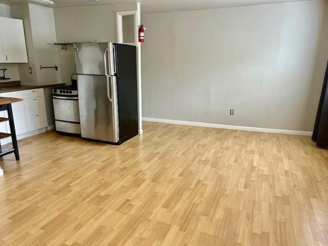 kitchen with light hardwood / wood-style flooring, range, white cabinetry, and stainless steel refrigerator