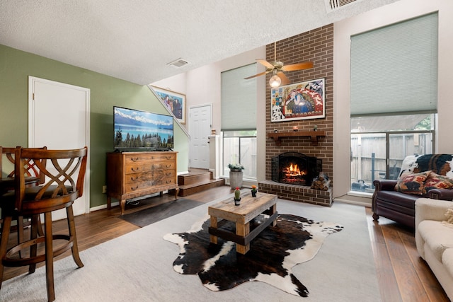 living room featuring a textured ceiling, ceiling fan, hardwood / wood-style floors, and a brick fireplace