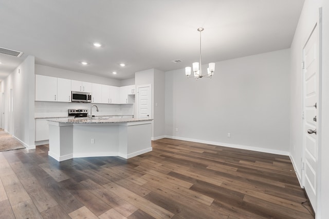 kitchen with dark hardwood / wood-style flooring, a center island with sink, hanging light fixtures, white cabinets, and appliances with stainless steel finishes