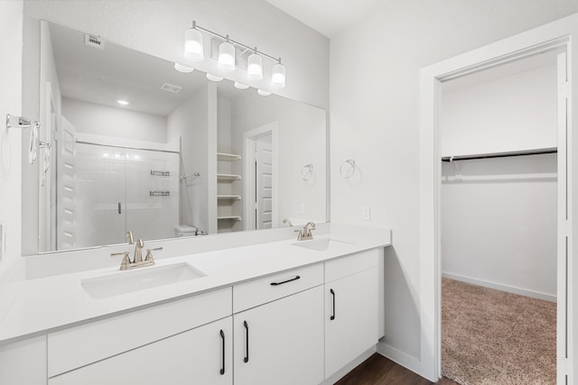 bathroom featuring a shower with door, dual vanity, wood-type flooring, and toilet