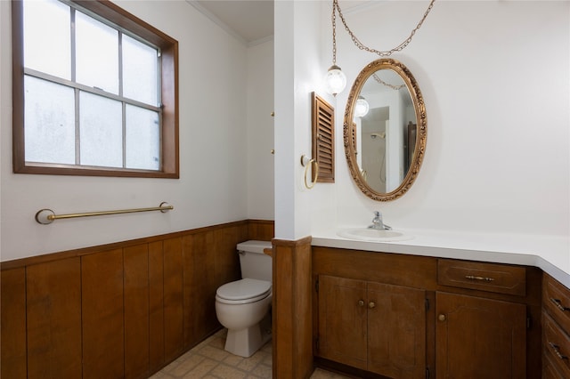 bathroom with ornamental molding, wooden walls, vanity, and toilet