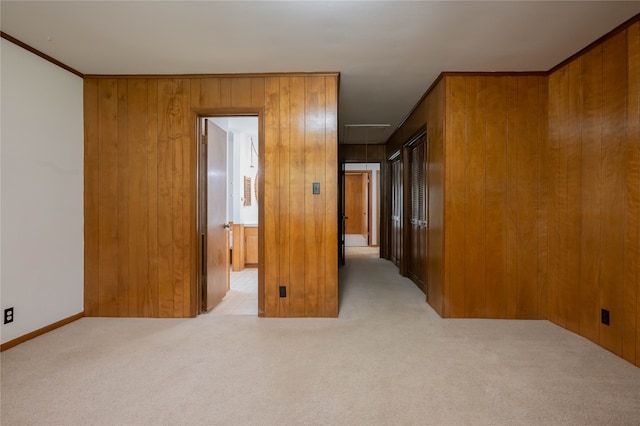 spare room with ornamental molding, wood walls, and light colored carpet