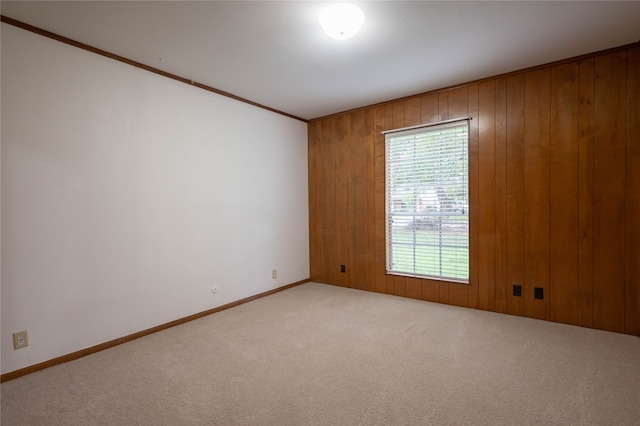 empty room with ornamental molding, wooden walls, and light carpet