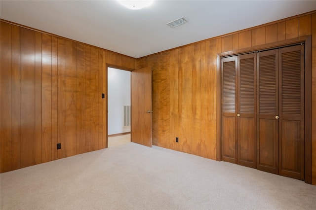 unfurnished bedroom featuring wooden walls, light colored carpet, and a closet