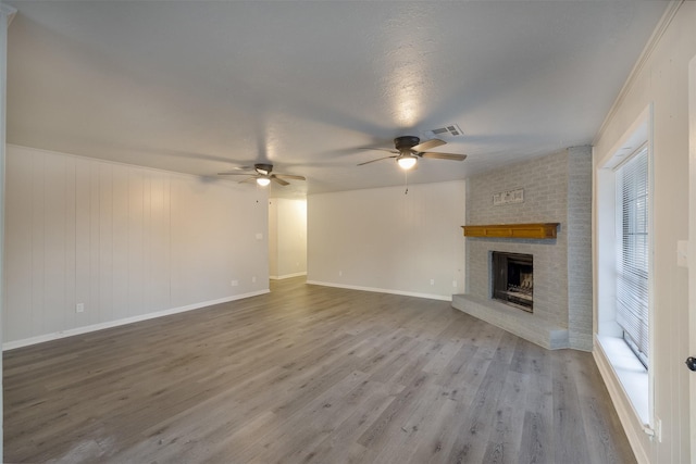 unfurnished living room with ceiling fan, wood-type flooring, a brick fireplace, and a textured ceiling