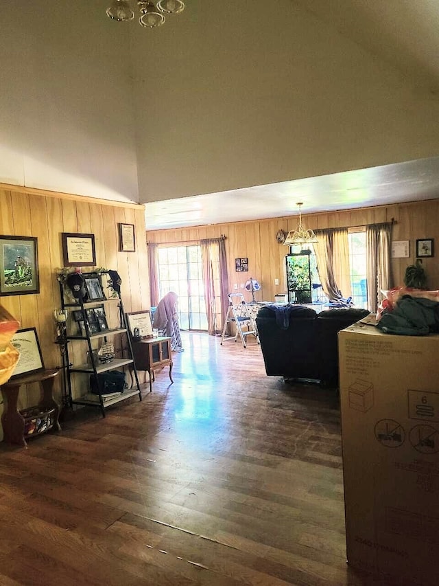 living room with dark hardwood / wood-style floors, wooden walls, a towering ceiling, and an inviting chandelier