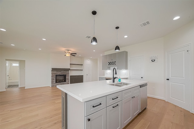 kitchen featuring light hardwood / wood-style floors, a center island with sink, a stone fireplace, sink, and ceiling fan