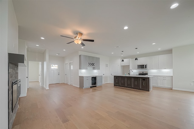 unfurnished living room featuring a fireplace, ceiling fan, wine cooler, light wood-type flooring, and sink