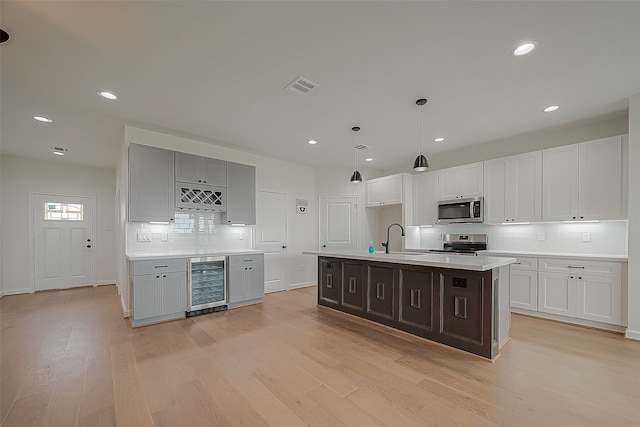 kitchen featuring light hardwood / wood-style floors, beverage cooler, stove, an island with sink, and sink