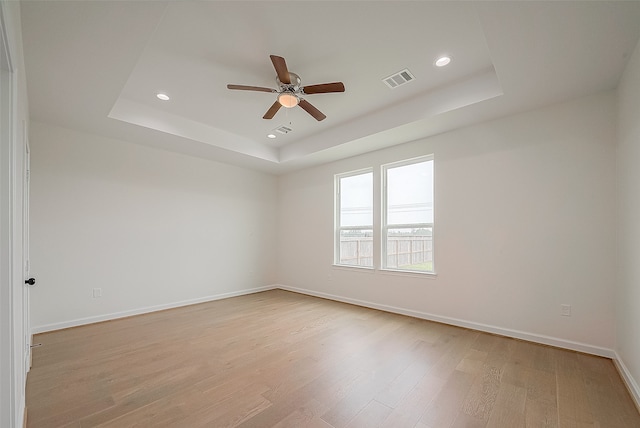 unfurnished room featuring ceiling fan, a raised ceiling, and light wood-type flooring