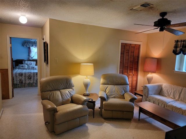 living room with a textured ceiling, carpet flooring, and ceiling fan