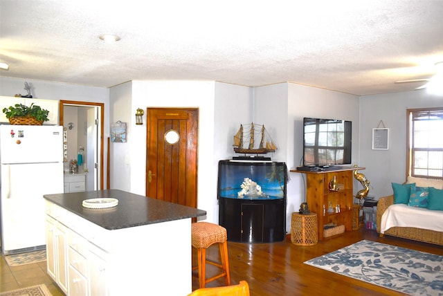 kitchen featuring white cabinetry, a textured ceiling, a kitchen island, white refrigerator, and light tile floors