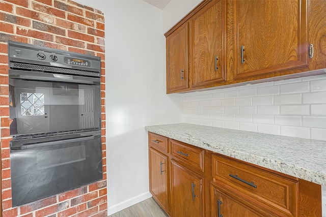 kitchen with light stone countertops, tasteful backsplash, light wood-type flooring, brick wall, and double oven