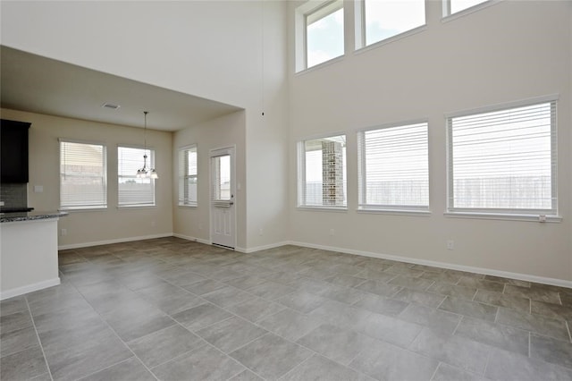 unfurnished living room featuring a notable chandelier, plenty of natural light, and light tile floors