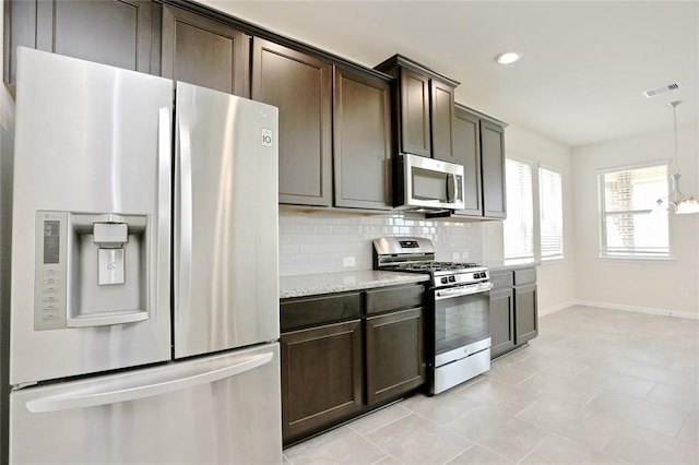 kitchen featuring light stone counters, backsplash, dark brown cabinets, appliances with stainless steel finishes, and light tile floors