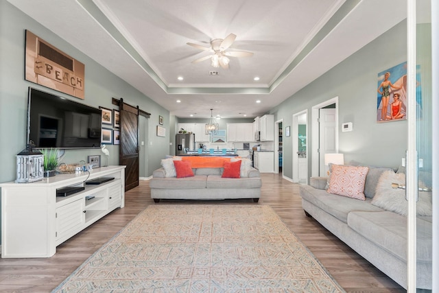 living room featuring light hardwood / wood-style floors, a raised ceiling, ceiling fan, crown molding, and a barn door