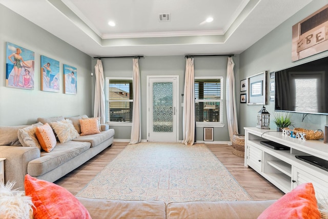 living room with a raised ceiling, ornamental molding, and light hardwood / wood-style floors