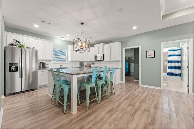 kitchen featuring white cabinets, a center island, decorative light fixtures, a kitchen bar, and stainless steel appliances