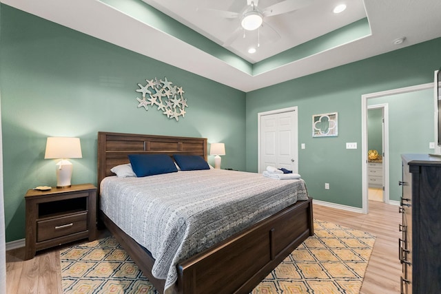 bedroom featuring a closet, ceiling fan, light hardwood / wood-style floors, and a tray ceiling