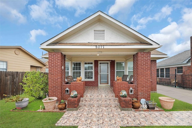 view of front facade featuring a porch, fence, brick siding, and a front yard