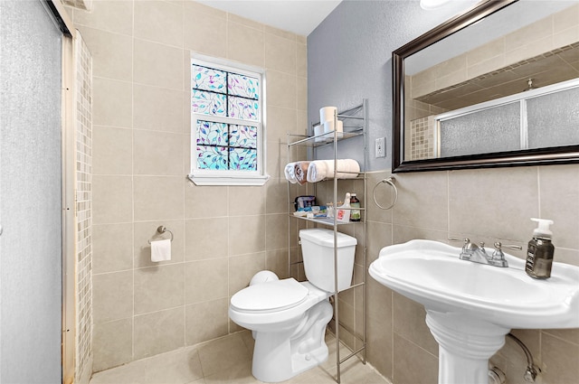 bathroom with tile walls, tile patterned flooring, a shower with shower door, and toilet