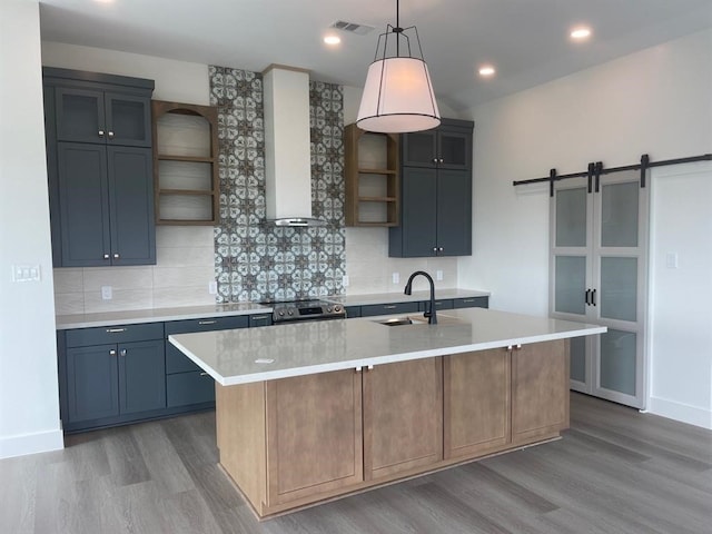 kitchen featuring light hardwood / wood-style floors, a kitchen island with sink, backsplash, and wall chimney exhaust hood