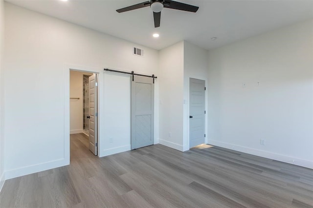 unfurnished bedroom with a walk in closet, hardwood / wood-style flooring, a barn door, a closet, and ceiling fan