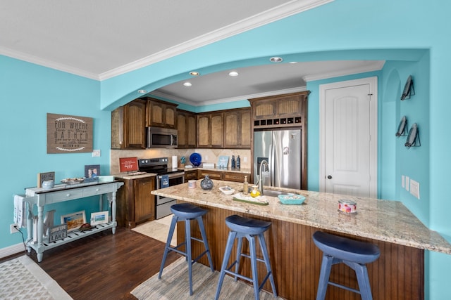 kitchen featuring dark hardwood / wood-style floors, a kitchen breakfast bar, backsplash, ornamental molding, and appliances with stainless steel finishes