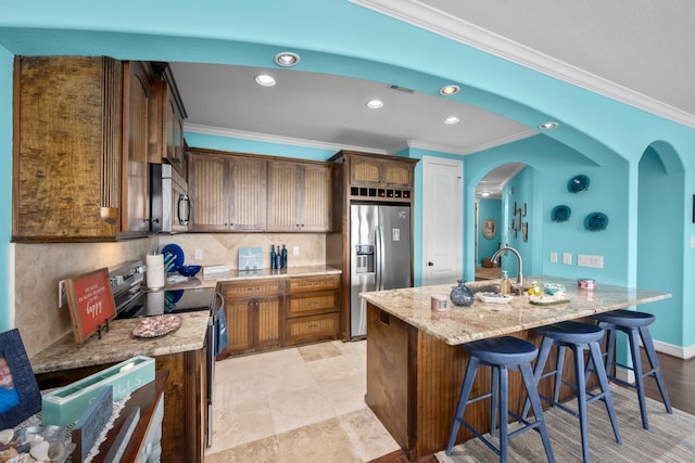 kitchen with an island with sink, light stone countertops, tasteful backsplash, and appliances with stainless steel finishes