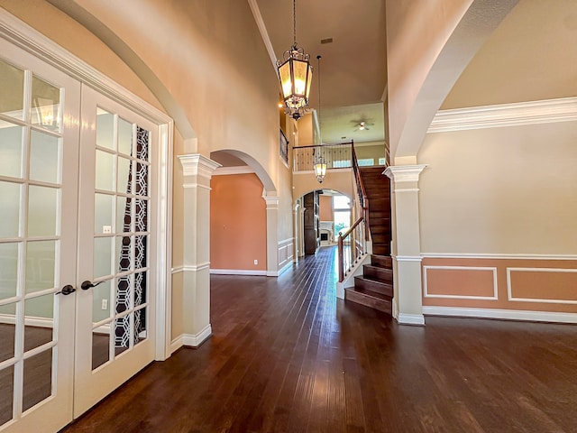 foyer featuring a chandelier, ornamental molding, dark wood-type flooring, ornate columns, and french doors