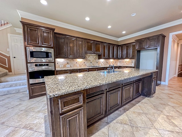 kitchen with an island with sink, appliances with stainless steel finishes, light stone countertops, and ornamental molding