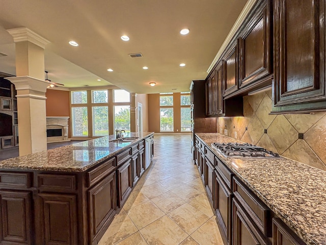 kitchen featuring a kitchen island, a high end fireplace, stainless steel gas stovetop, backsplash, and light tile flooring