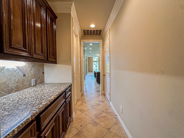 kitchen featuring crown molding, dark stone countertops, dark brown cabinetry, tasteful backsplash, and light tile floors