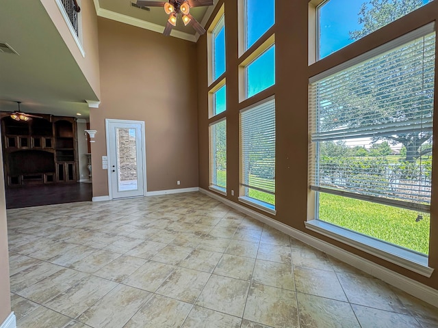 unfurnished living room featuring tile flooring, ceiling fan, a high ceiling, and ornamental molding