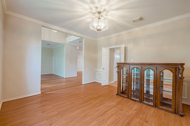 spare room with ornamental molding, a notable chandelier, and light hardwood / wood-style flooring