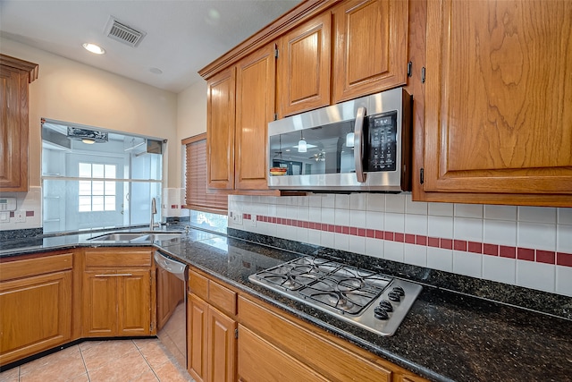 kitchen with stainless steel appliances, light tile patterned floors, tasteful backsplash, dark stone counters, and sink